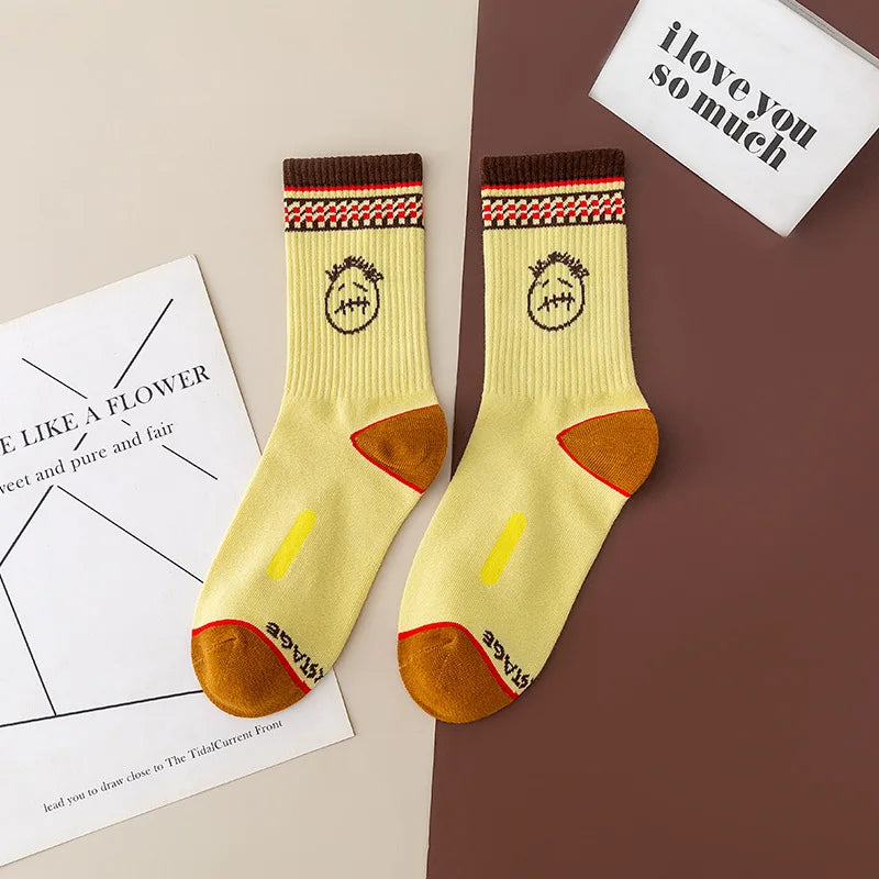Pale yellow crew socks with brown cuffs, patterned bands, ochre heels and toes and black face graphics.