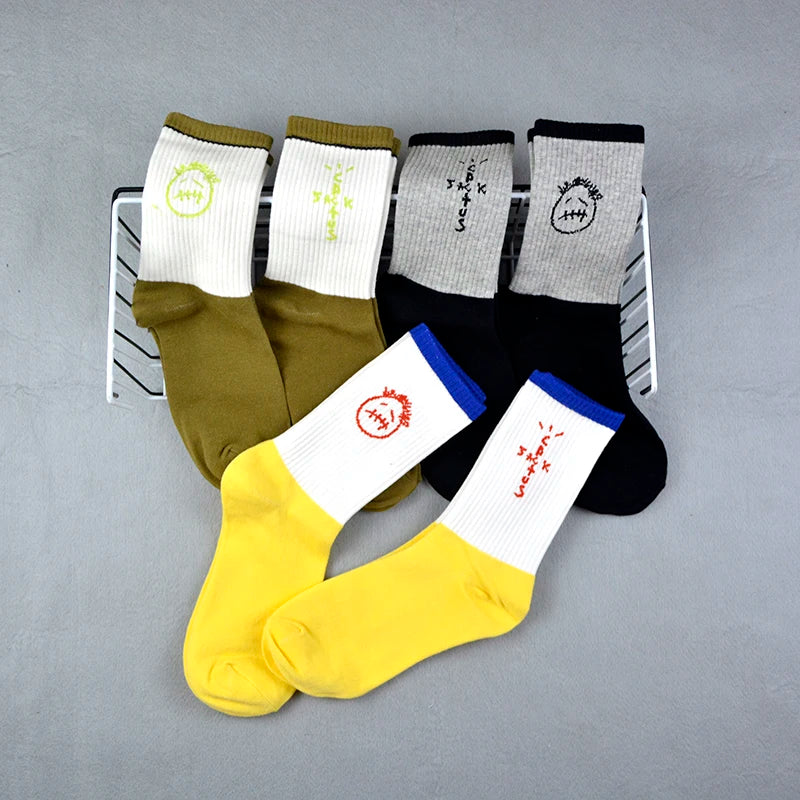 Olive, black and yellow color-block socks with face and lettering graphics arranged around a wire basket.