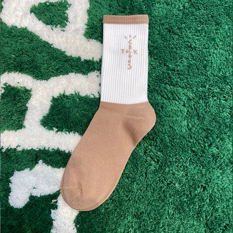 White and tan crew sock with tan cross-shaped lettering, side view on a green rug