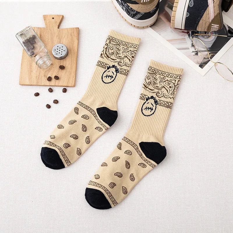 Cream crew socks with dark paisley patterns, stitched-face graphics, and black heels and toes, flat lay