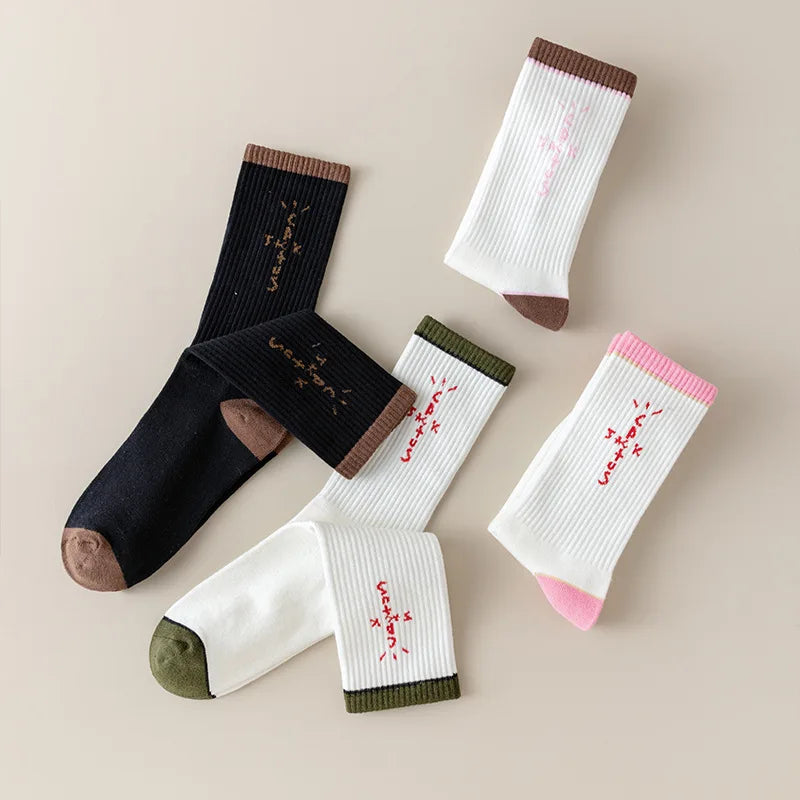 Folded black and white socks with cross-shaped lettering and brown, olive and pink accents.