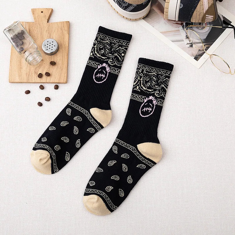 Black crew socks with cream paisley patterns, stitched-face graphics, and cream heels and toes, flat lay