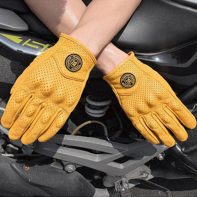 Yellow gloves with a brand logo worn by a person on a motorcycle, emphasizing ventilation and breathability.