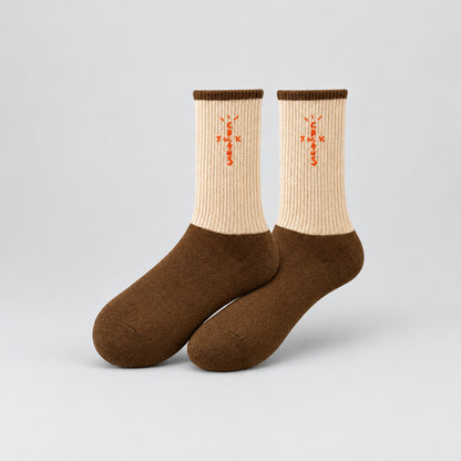 Cream and brown crew socks with orange cross-shaped lettering and brown cuffs, angled view