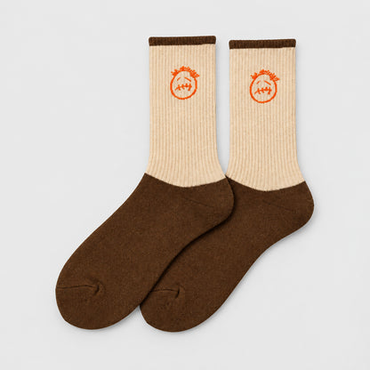 Cream and brown crew socks with orange stitched-face graphics and brown cuffs, angled view