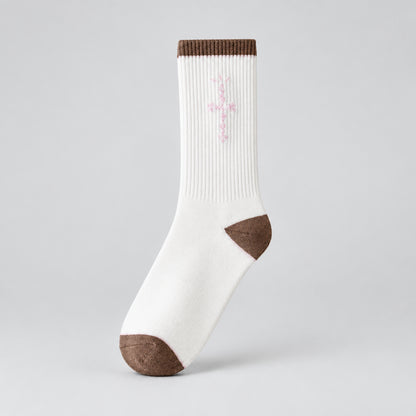 White crew sock with pale pink cross-shaped lettering and brown cuff, heel, and toe, angled view