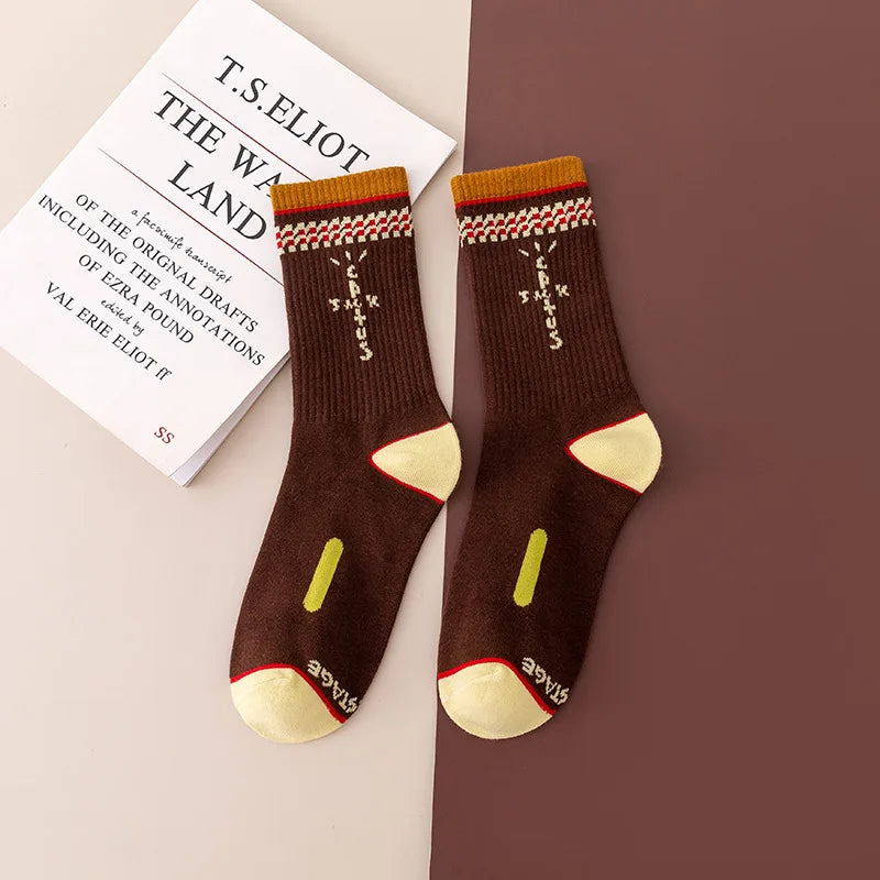 Brown crew socks with cream cross-shaped lettering, patterned cuffs, and cream heels and toes, flat lay