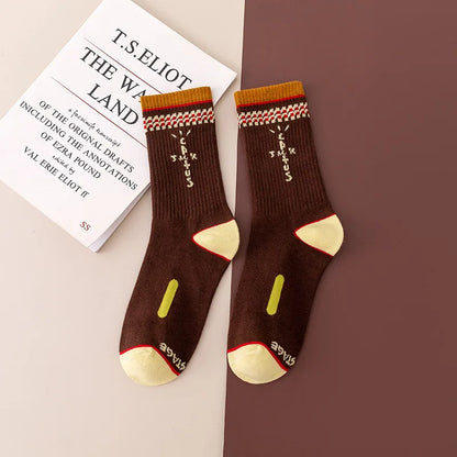 Brown crew socks with cream cross-shaped lettering, patterned cuffs, and cream heels and toes, flat lay