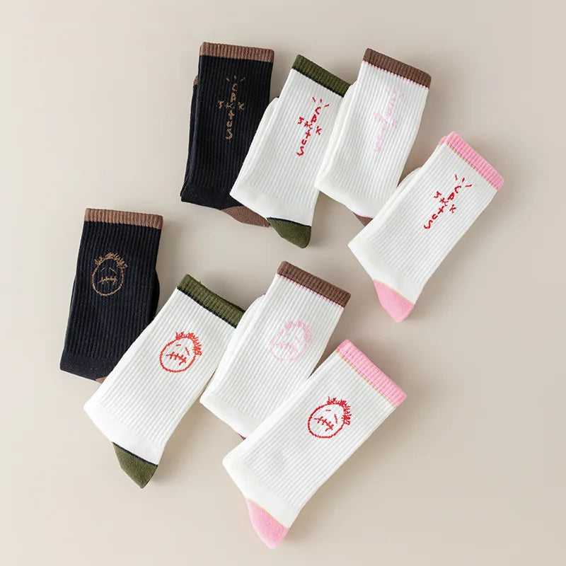 Folded black and white socks displaying face and lettering designs with brown, olive and pink accents.