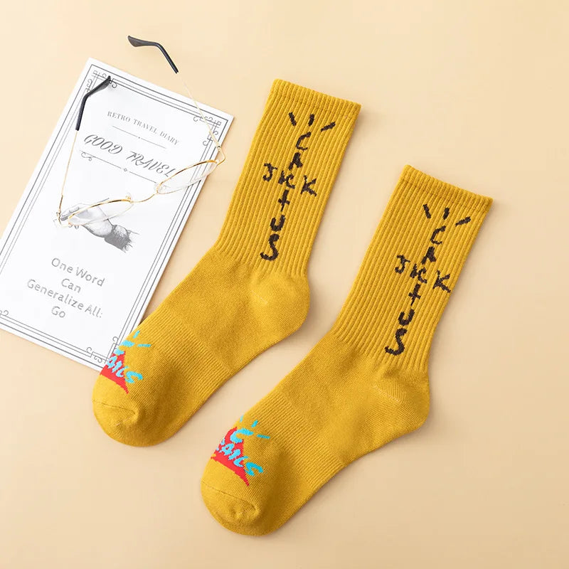 Mustard yellow crew socks with dark cross-shaped lettering and colorful toe graphics, flat lay