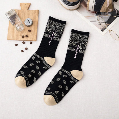 Black crew socks with cream paisley patterns, cross-shaped lettering, and cream heels and toes, flat lay