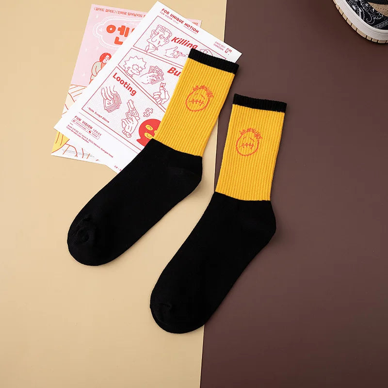 Yellow and black crew socks laid flat with black cuffs and orange face graphics.