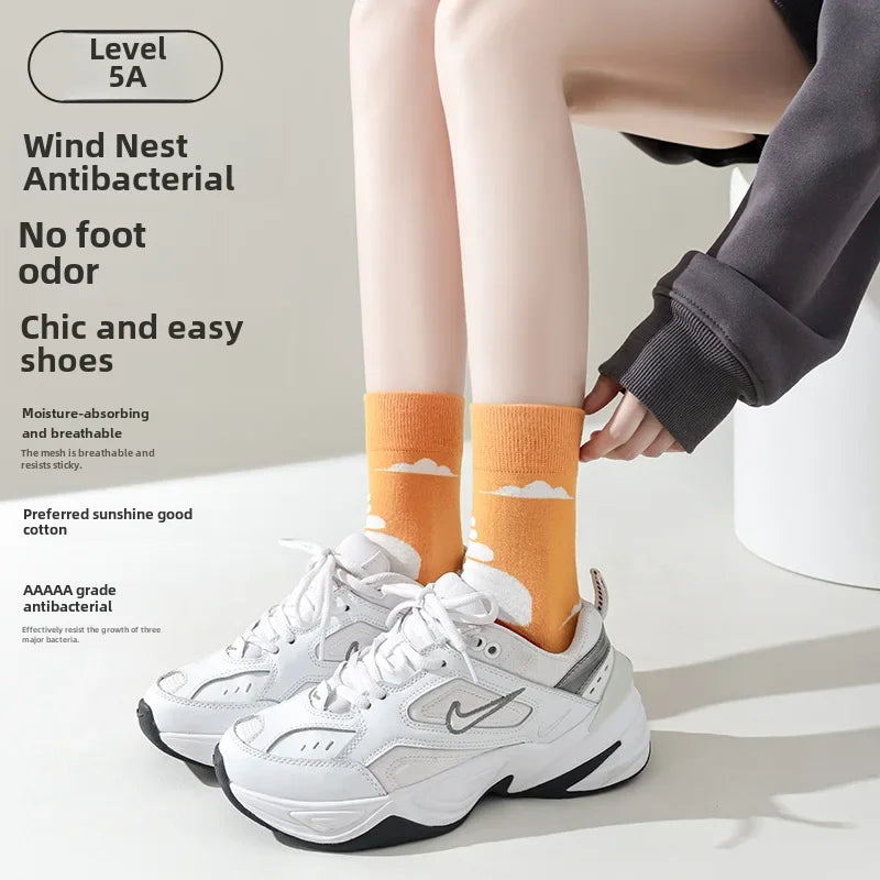 Person wearing white sneakers with orange socks on a light background