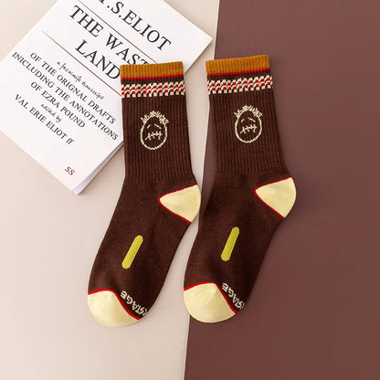 Brown crew socks with cream stitched-face graphics, patterned cuffs, and cream heels and toes, flat lay