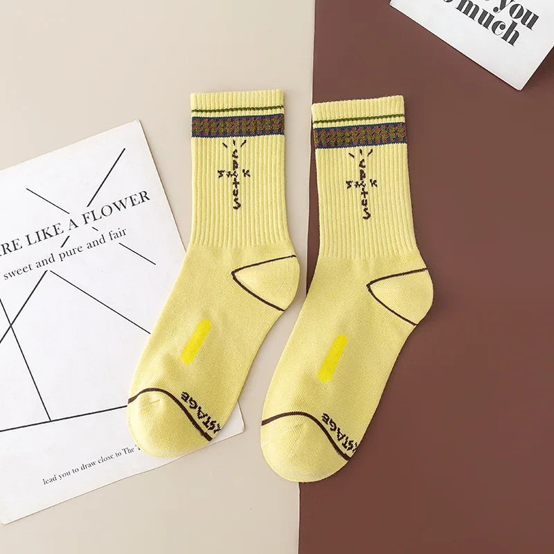 Pale yellow crew socks with dark cross-shaped lettering and patterned cuff stripes, flat lay