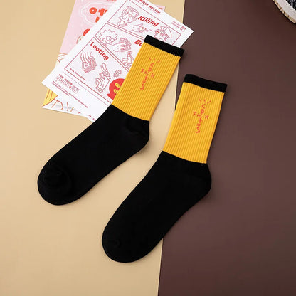 Yellow and black crew socks laid flat with black cuffs and orange cross-shaped lettering.