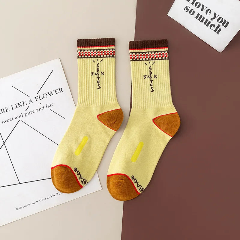 Pale yellow crew socks with brown cuffs, patterned bands, ochre heels and toes and black cross-shaped lettering.