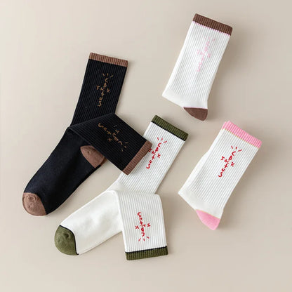 Folded black and white socks with cross-shaped lettering and brown, olive and pink accents.