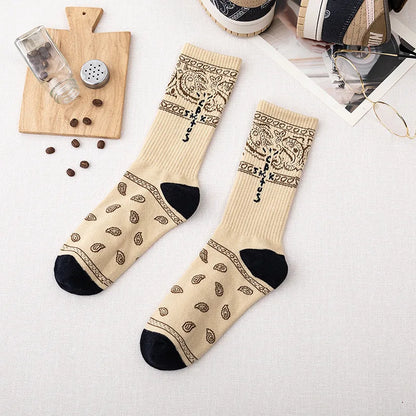 Cream crew socks with dark paisley patterns, cross-shaped lettering, and black heels and toes, flat lay