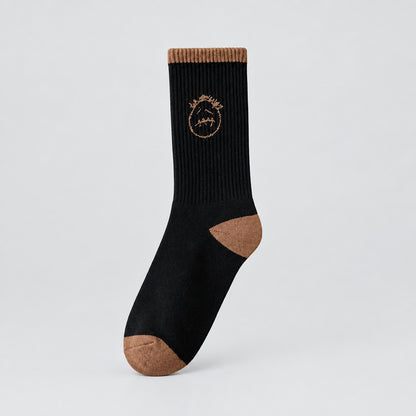 Black crew sock with a tan stitched-face graphic and tan cuff, heel, and toe, angled view