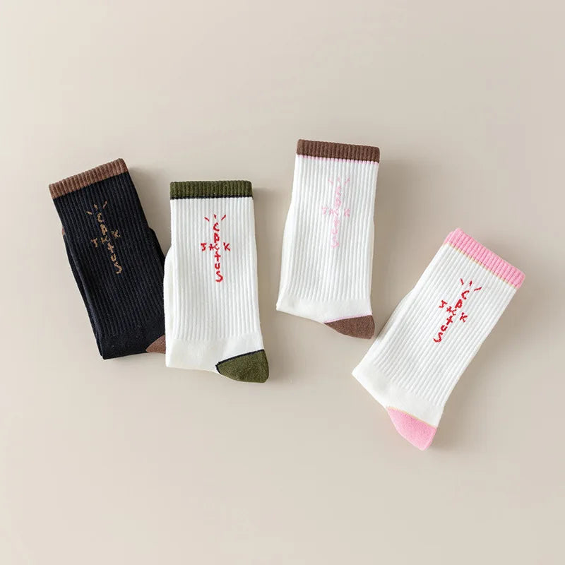 Four folded black and white socks with cross-shaped lettering and brown, olive and pink cuffs.