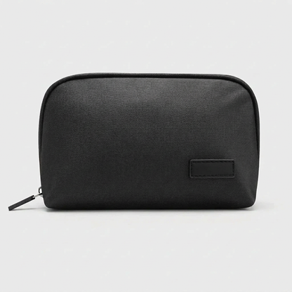 Black tech organizer pouch shown closed with zipper pull and plain stitched patch on a white studio background.